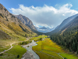 A beautiful landscape of the Barskoon valley with a river meandering through lush green meadows,...