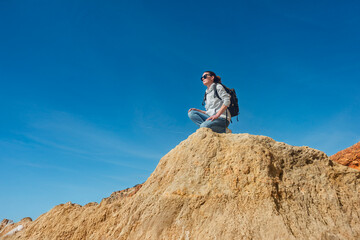 Female Hiker Sitting on Cliff Edge Enjoying Scenic Views Under Clear Blue Sky