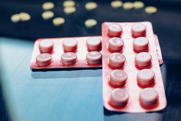 Two blister packs containing white round tablets are placed on a reflective surface, with some...