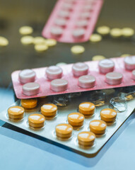 Blister packs of various pills, including orange and pink ones, are displayed against a reflective...