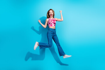 Energetic young woman jumping with excitement on a vibrant blue background, expressing fun, style,...