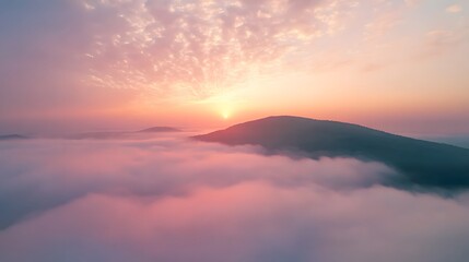 Fototapeta premium Aerial view of a mountain covered in fog under pastel morning hues