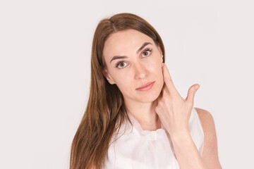 Caucasian young adult female with long brown hair touching face on neutral background.