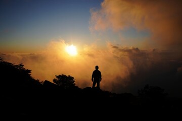 Silhouette of a Person Standing on a Mountain Peak at Sunset Over Clouds