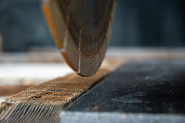 A saw blade approaches wooden planks in a workshop, capturing the moment of precision cutting with...