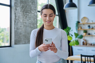 Young woman standing at home using smartphone