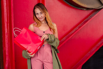 Stylish woman holding shopping bag in front of red wall