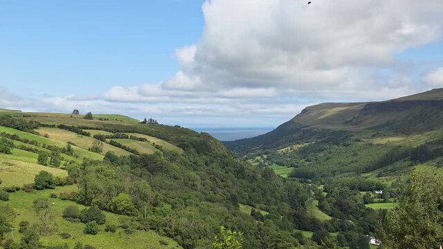 Time lapse with grasses in the foreground with sweeping vistas of Glenariff, Queen of the Glens, verdant hills, and a valley stretching toward the sea in Northern Ireland.