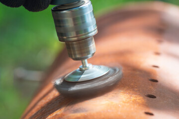 A worker removes rust and corrosion from a metal surface using a wire brush attachment on an...
