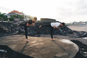 Two men performing warrior III pose in synchronized motion, embodying discipline, strength and...