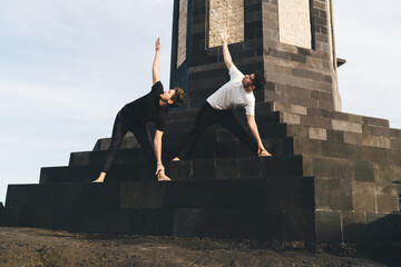 Two young men holding triangle yoga pose in urban symmetry, expressing concentration, discipline,...