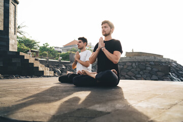 Two young men in lotus position with prayer hands in anjali mudra, symbolizing mindful intention,...
