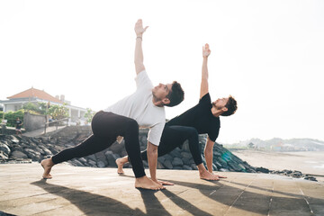 Two young men perform revolved side angle pose in unison, illustrating digital era resilience, flexibility, and conscious balance through dynamic movement and synchronized body-mind control.