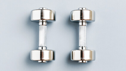 Two dumbbells, silver in color on a gray background, top view, flat lay. Minimalist style. High-resolution photo