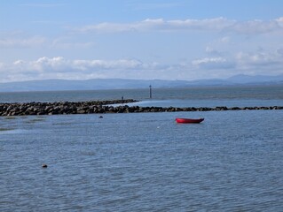 A small red wooden boat tied to a moorings wating to be rowed to shore as the vessel returns.