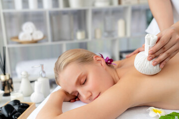 Hot herbal ball spa massage body treatment, masseur gently compresses herb bag on woman body....