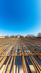 Obraz premium Reinforcement steel bars create a grid pattern for concrete. An excavator operates under a clear blue sky.