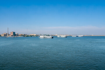 Obraz premium Serene view of cruise ships entering Esna Lock along the Nile River in Egypt under clear blue sky with distant city skyline and minarets.