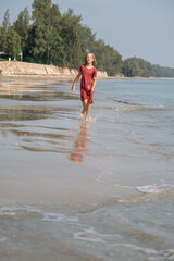 A teenage girl joyfully walks along the sandy beach, her wet dress glistening in the sunlight. The...
