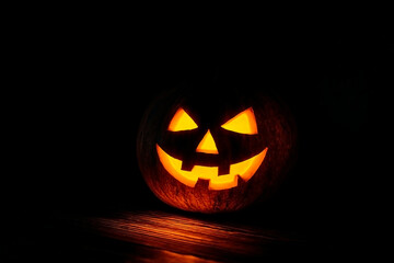 Halloween night with glowing jack-o’-lantern on wood, surrounded by deep shadows and mystery
