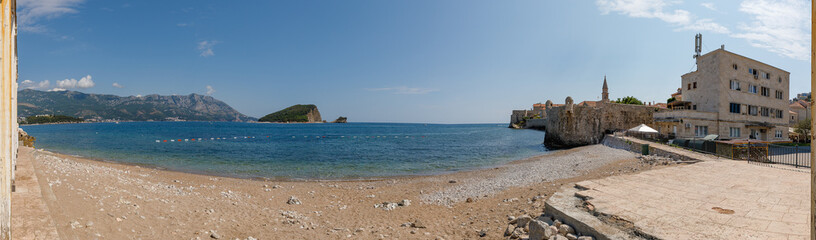 Obraz premium Breathtaking Panoramic View of the Adriatic Coastline in Montenegro, Showcasing a Sandy Beach, Historic Buildings, and Majestic Mountains Under a Clear Blue Sky
