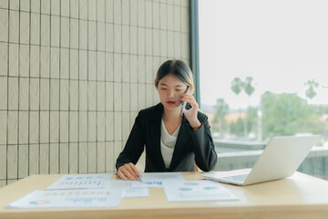 Asian female accountant stressed while finalizing financial reports, holding head in frustration.