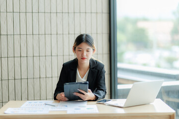 Asian female accountant reviewing annual business revenue reports with focus and professionalism.