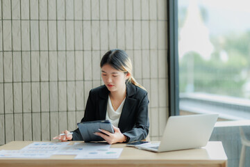 Asian female accountant reviewing annual business revenue reports with focus and professionalism.