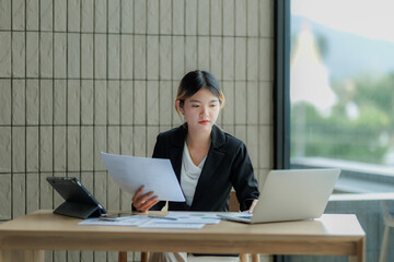 Dedicated Asian accountant summarizing annual income figures using laptop and paperwork.