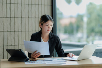 Dedicated Asian accountant summarizing annual income figures using laptop and paperwork.