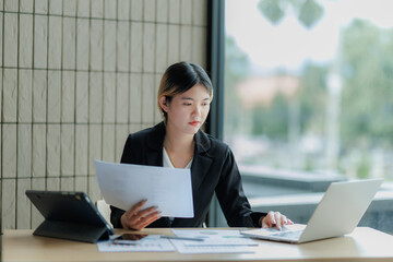 Dedicated Asian accountant summarizing annual income figures using laptop and paperwork.