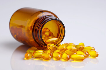 Amber pill bottle with yellow soft gel capsules spilling onto white surface