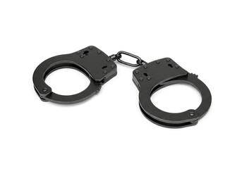 A pair of black metal handcuffs connected by a chain laying on a plain white surface in a studio shot