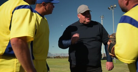 Coach with diverse baseball players speaking in huddle on field, slapping gloves boosting morale