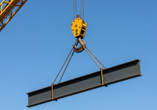 A crane lifting a steel beam against a clear blue sky during construction work at a building site