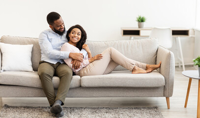 Happy Loving Family. Beautiful african american couple spending weekend together, resting on the couch indoors at home in living room, relaxing and enjoying the company of each other, hugging