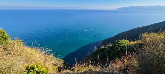 Crystal clear sea with mountain backdrop and green landscape