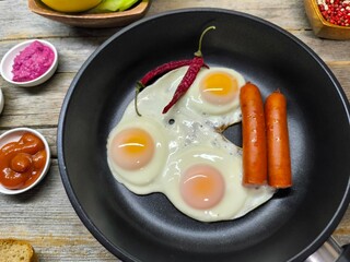 delicious appetizing breakfast of fried eggs and sausages on a frying pan