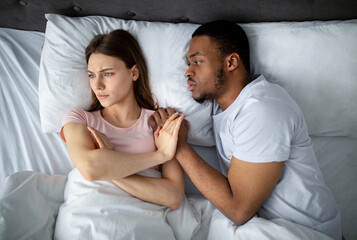 Sexual apathy concept. African American guy touching his upset girlfriend in bed, woman refusing...