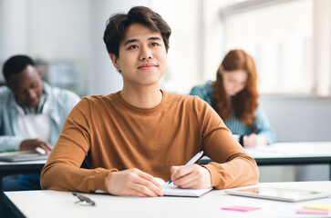 School's in Session. Portrait of cheerful happy asian male student sitting at table in academic...