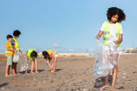 Busy diverse teenager people in uniform and black curly girl collect garbage and plastic bottles in bag on beach. Environment care, clean up, save planet, recycle, protect sea