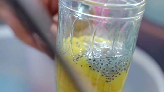 Close-up of yellow cendol dessert in a glass with basil seeds and syrup, ideal for tropical drink, summer refreshment, and authentic Southeast Asian beverage concepts.