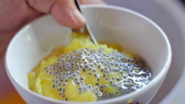 Close-up of yellow cendol dessert topped with fresh basil seeds in a white bowl, perfect for tropical sweet dish, traditional Southeast Asian food, and exotic culinary concepts.