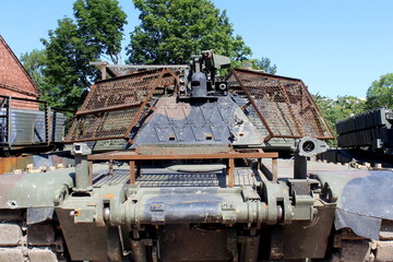 A rusty, damaged tank stands in the open air in the summer.