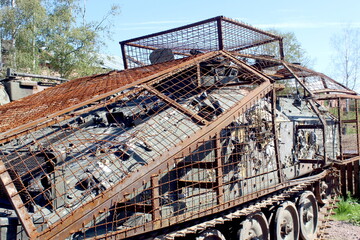 A rusty, damaged tank stands in the open air in the summer.