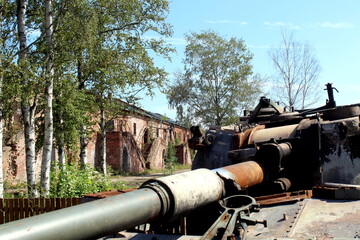 A rusty, damaged tank stands in the open air in the summer.