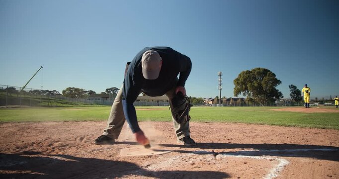 Brush sweeping chalk line at home plate, umpire donning face mask preparing to officiate pitch