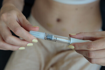 A Close-Up View of a Person Holding a Medical Injection Device, Featuring a Clear Syringe and Pale...