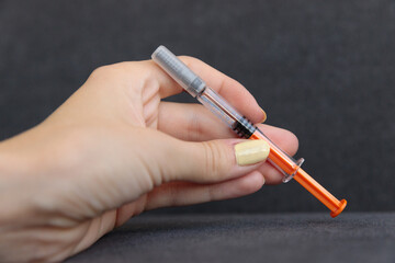 Close-Up View of a Hand Holding a Medical Syringe with an Orange Tip against a Dark Background for Exploration of Health and Medical Topics