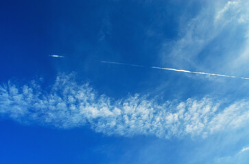 Blue sky crossed by contrail and scattered clouds
